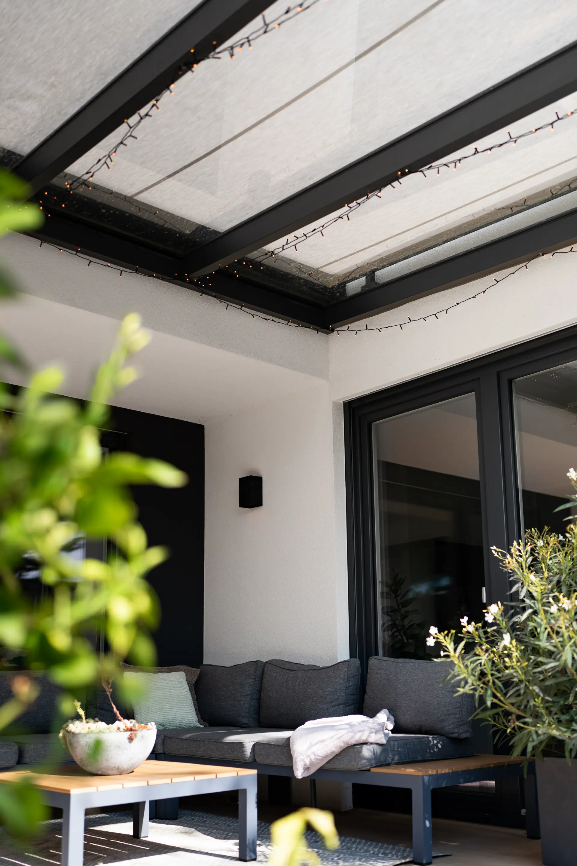 Terrassendach mit beige gestreiftem Sonnenschutz über einer Loungeecke mit Lichterkette