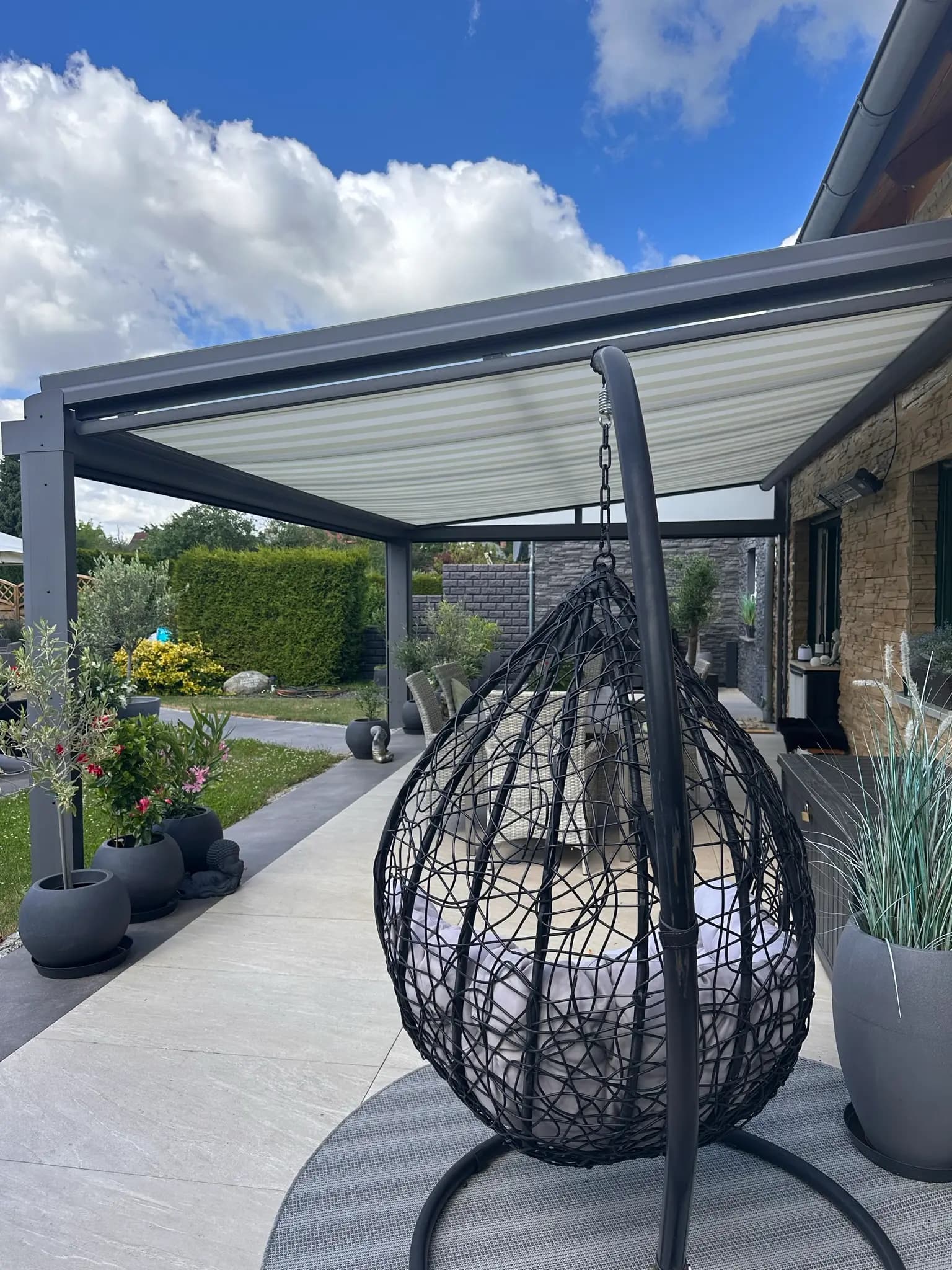 Terrasse mit Hängesessel und Loungemöbeln unter einem gestreiften Sonnenschutz-Screen