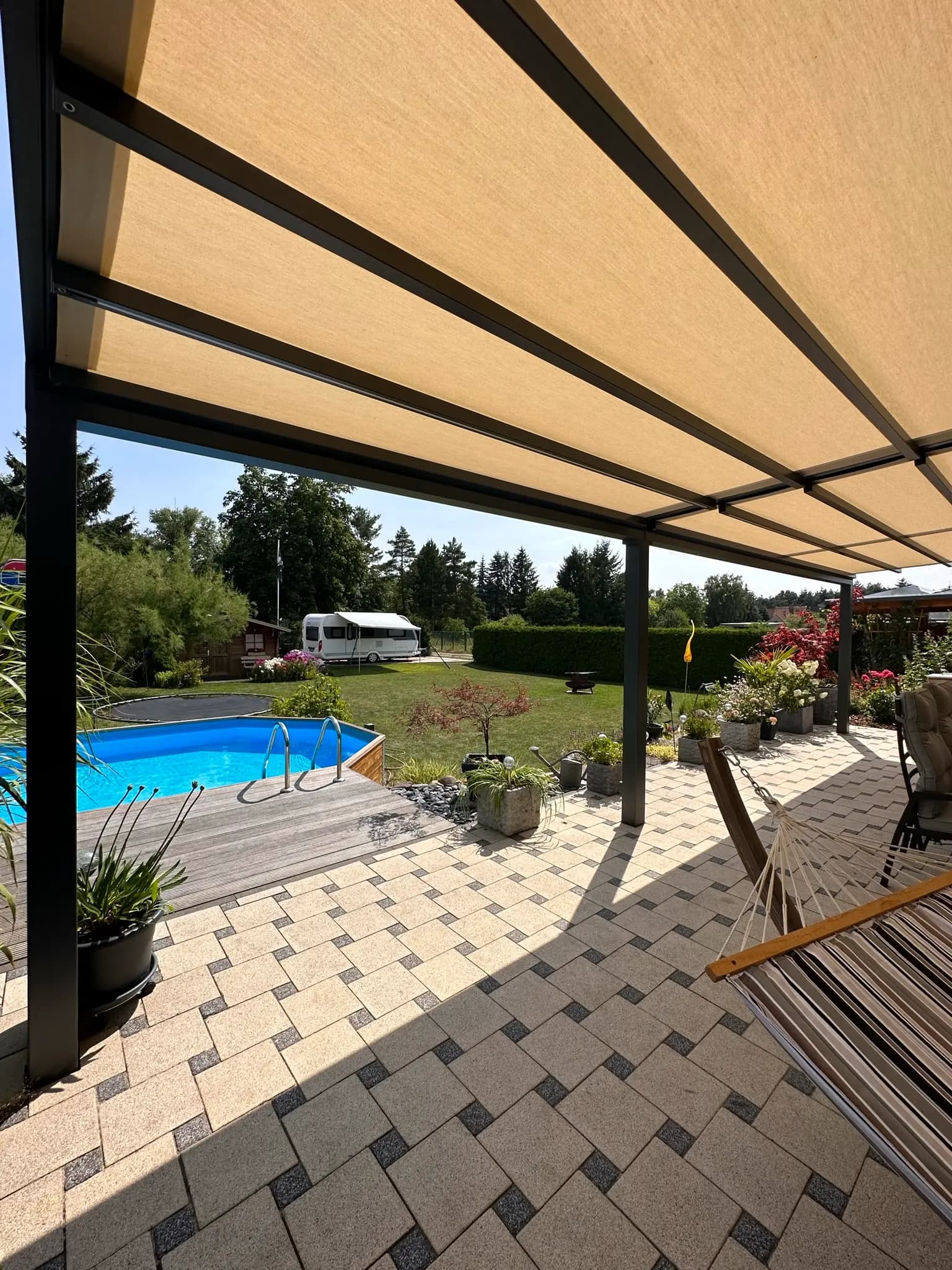 Terrasse mit ausgefahrener beiger Markise, dahinter Pool und Hängematte