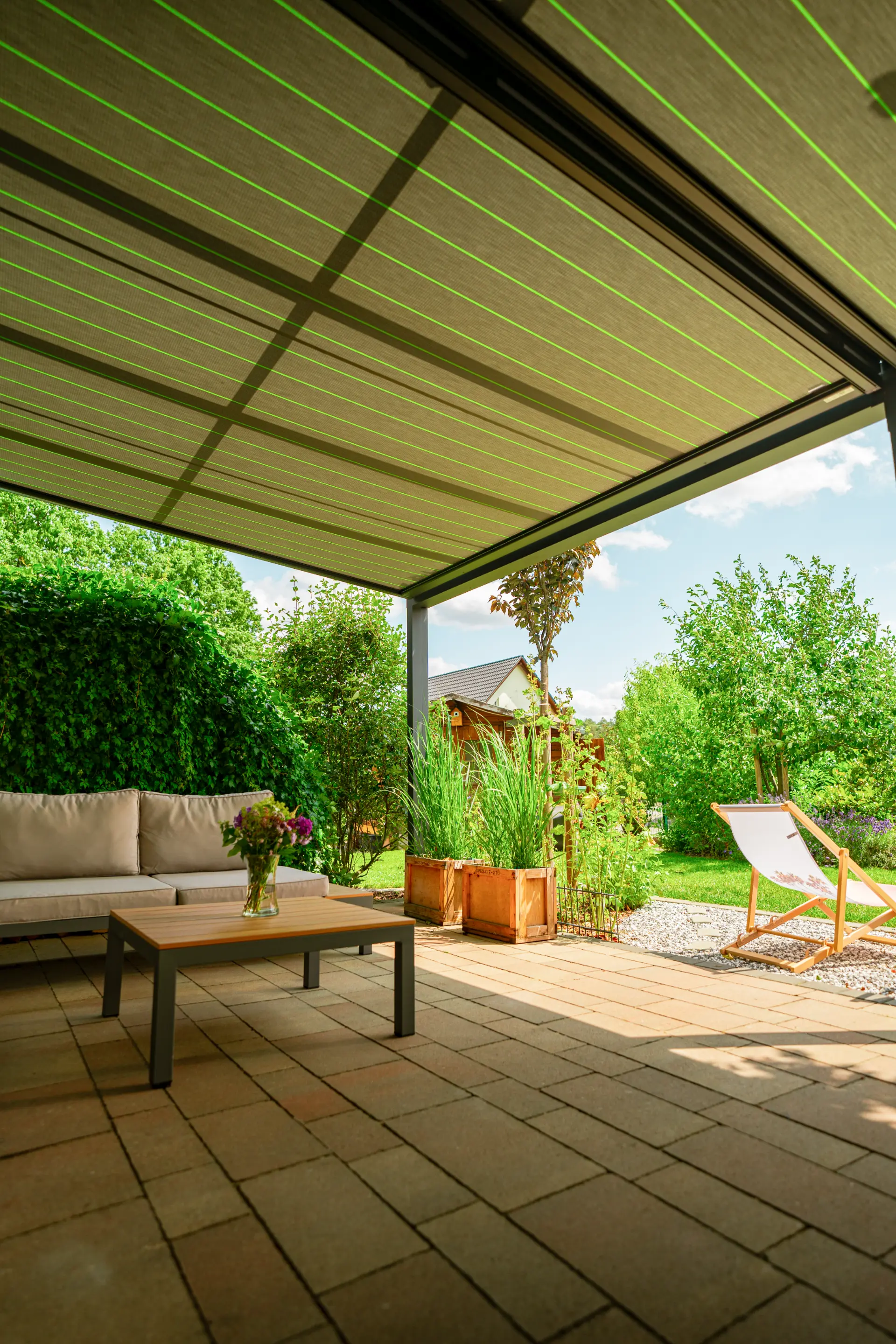 Terrassendach mit textilem Sonnenschutzdach über einer Gartenlounge