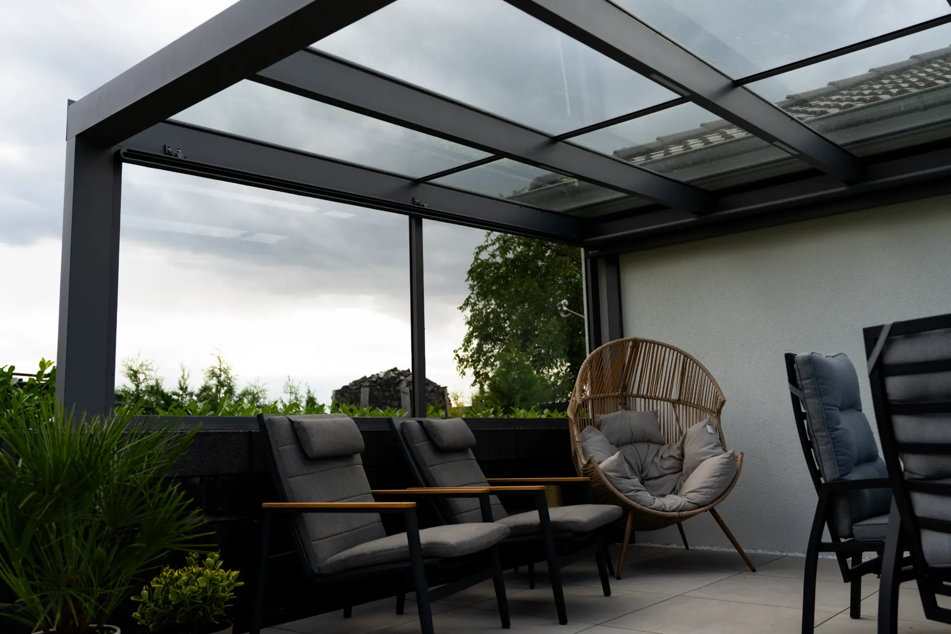 Terrassendach mit Glasdach über Loungemöbeln und einem Kokon-Sessel