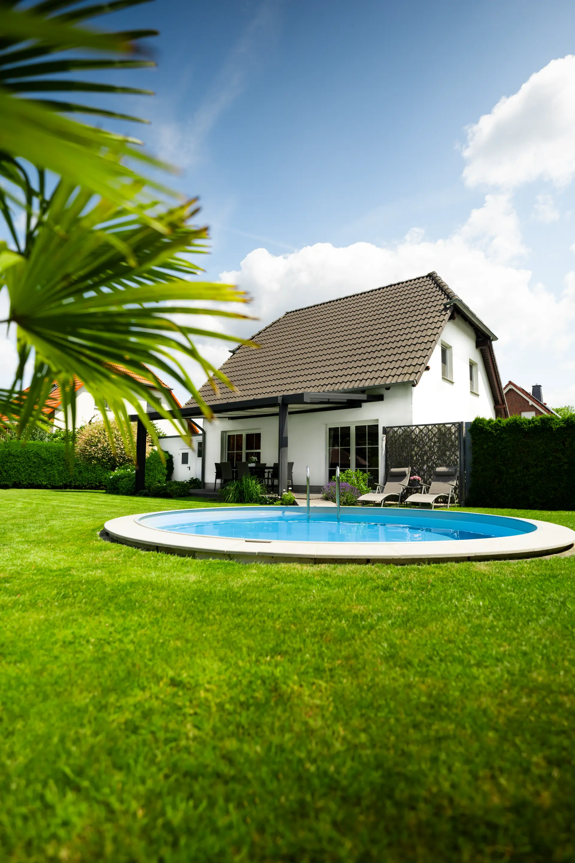 Weißes Einfamilienhaus mit angebautem Terrassendach, davor ein Rundpool im Rasen