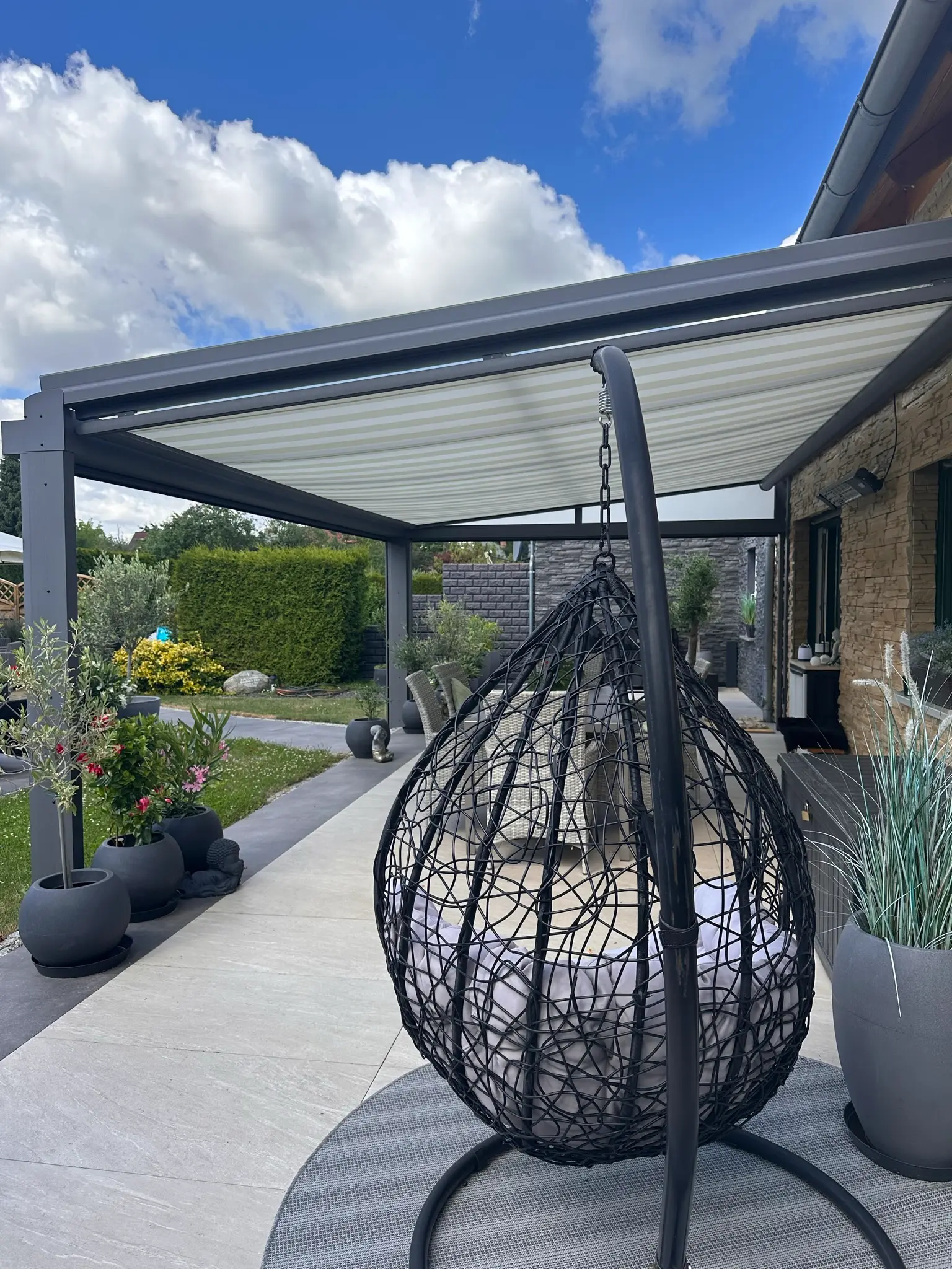 Terrasse mit Hängesessel und Loungemöbeln unter einem gestreiften Sonnenschutz-Screen