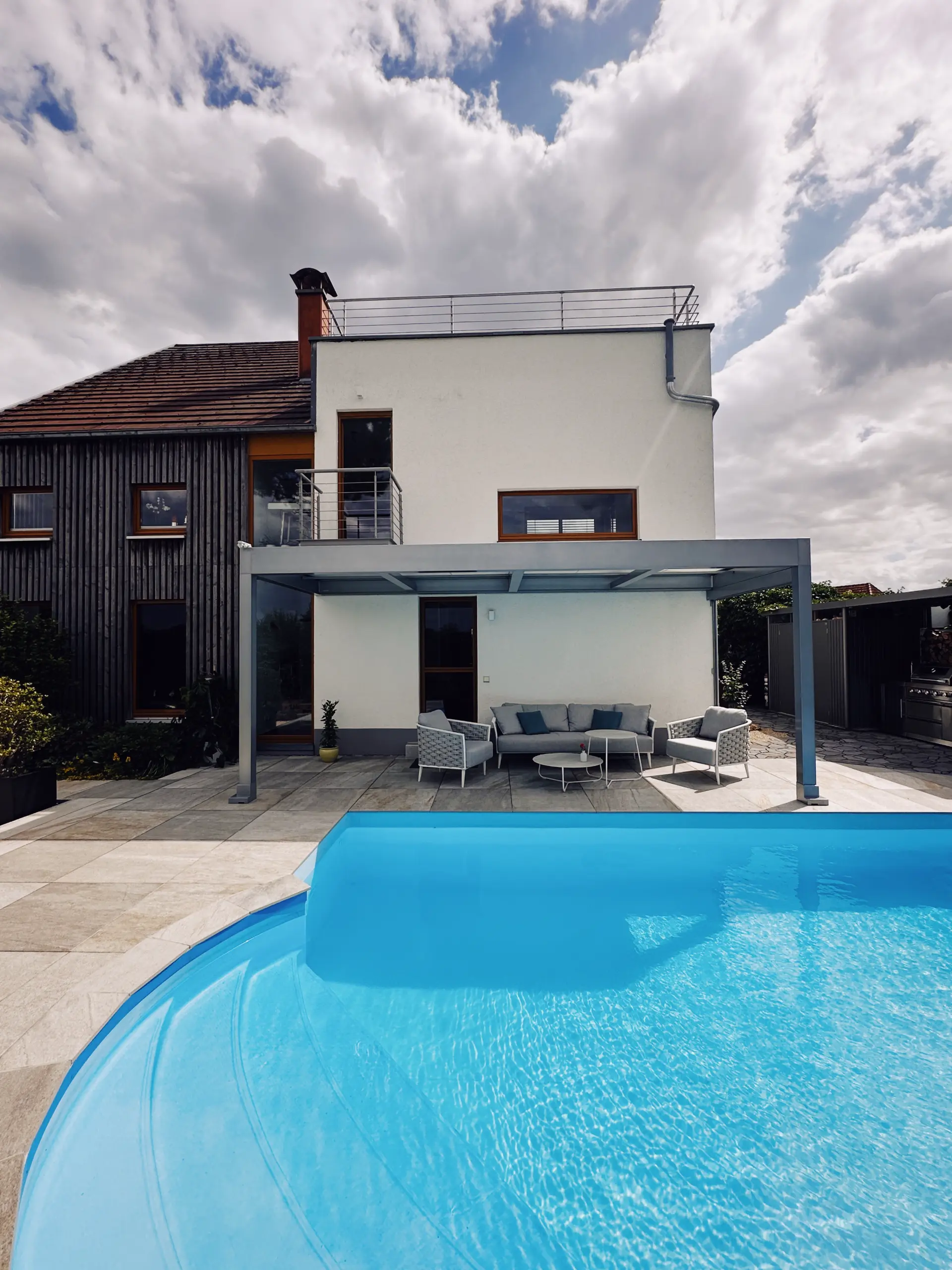 Modernes Wohnhaus mit grauem Terrassendach über dem Loungebereich, davor ein Pool