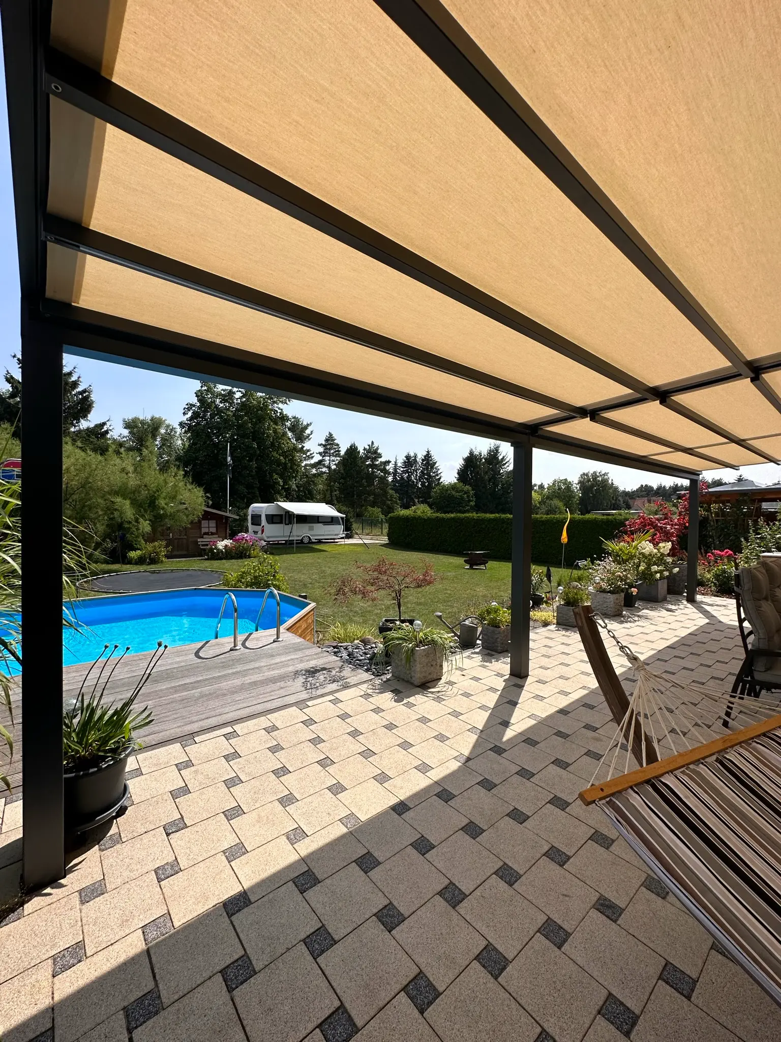 Terrasse mit ausgefahrener beiger Markise, dahinter Pool und Hängematte
