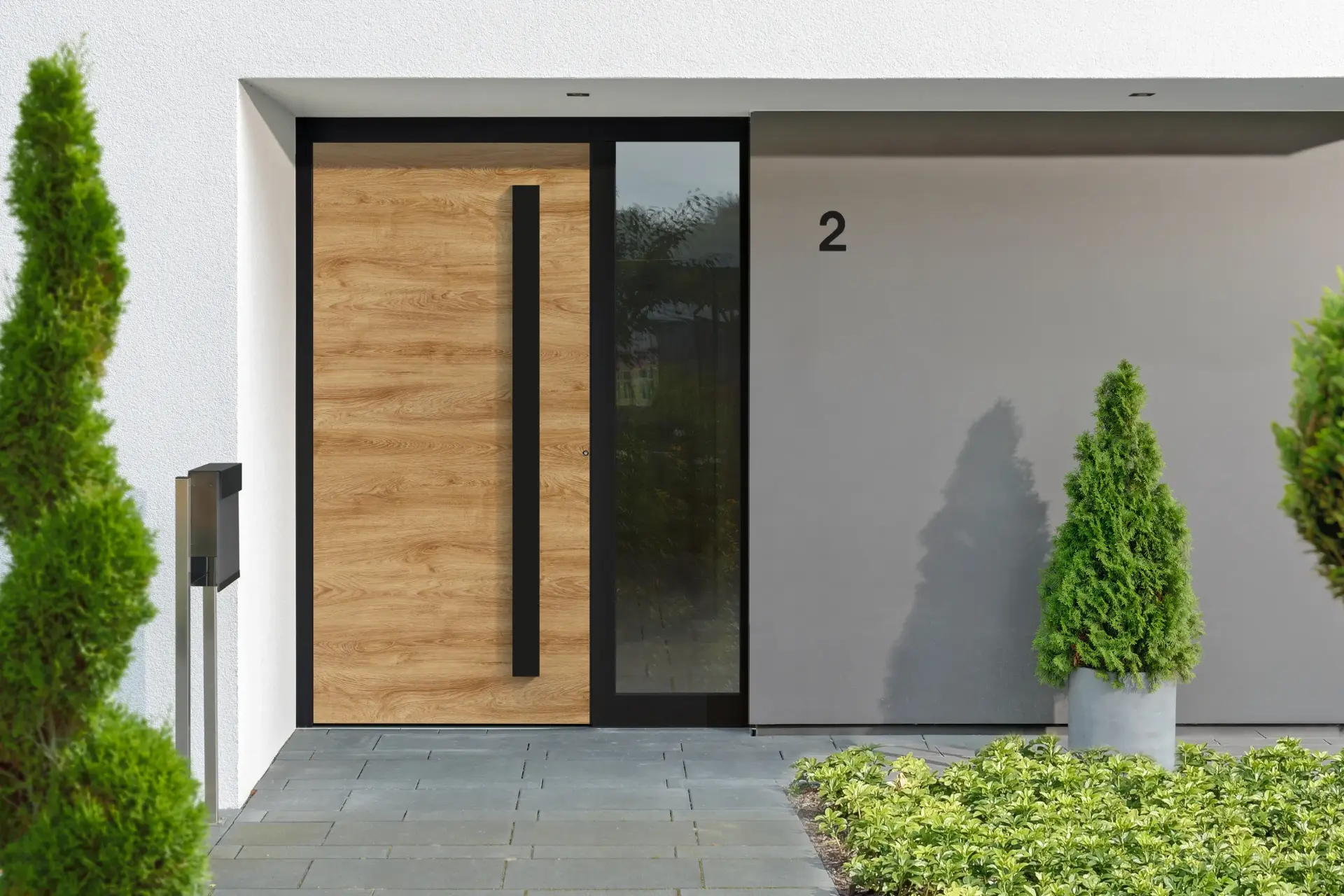 Haustür in Eiche-Holzoptik mit langem schwarzem Griff und schmalem Glas-Seitenteil, davor eine Säulenzypresse