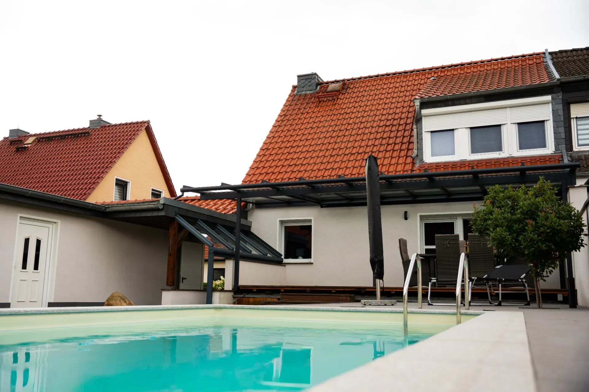 Terrassendach in Anthrazit an einem Wohnhaus, davor ein Pool mit Einstiegsleiter