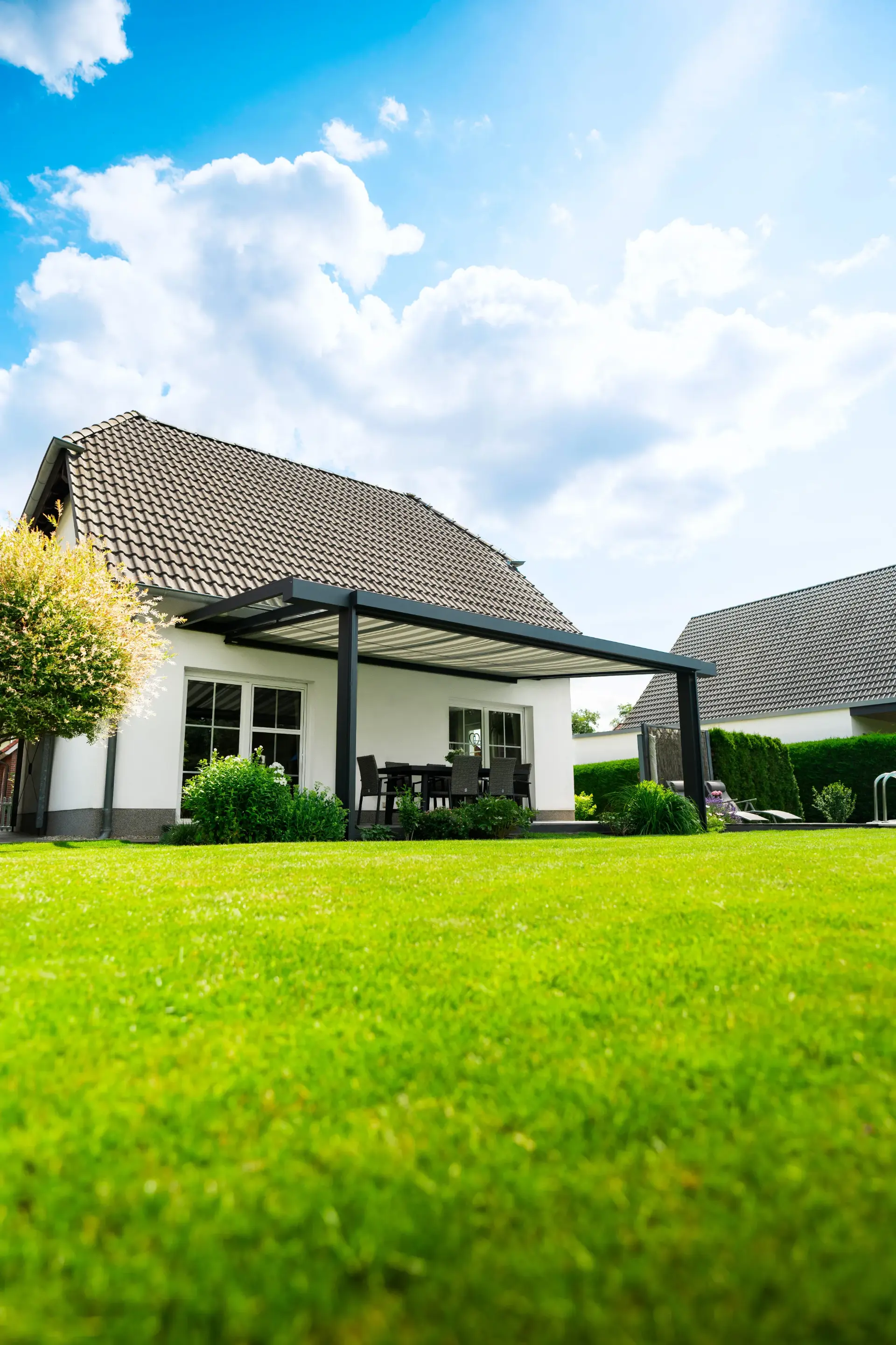 Terrassendach mit Glasdach an einem weißen Einfamilienhaus, davor ein gepflegter Rasen
