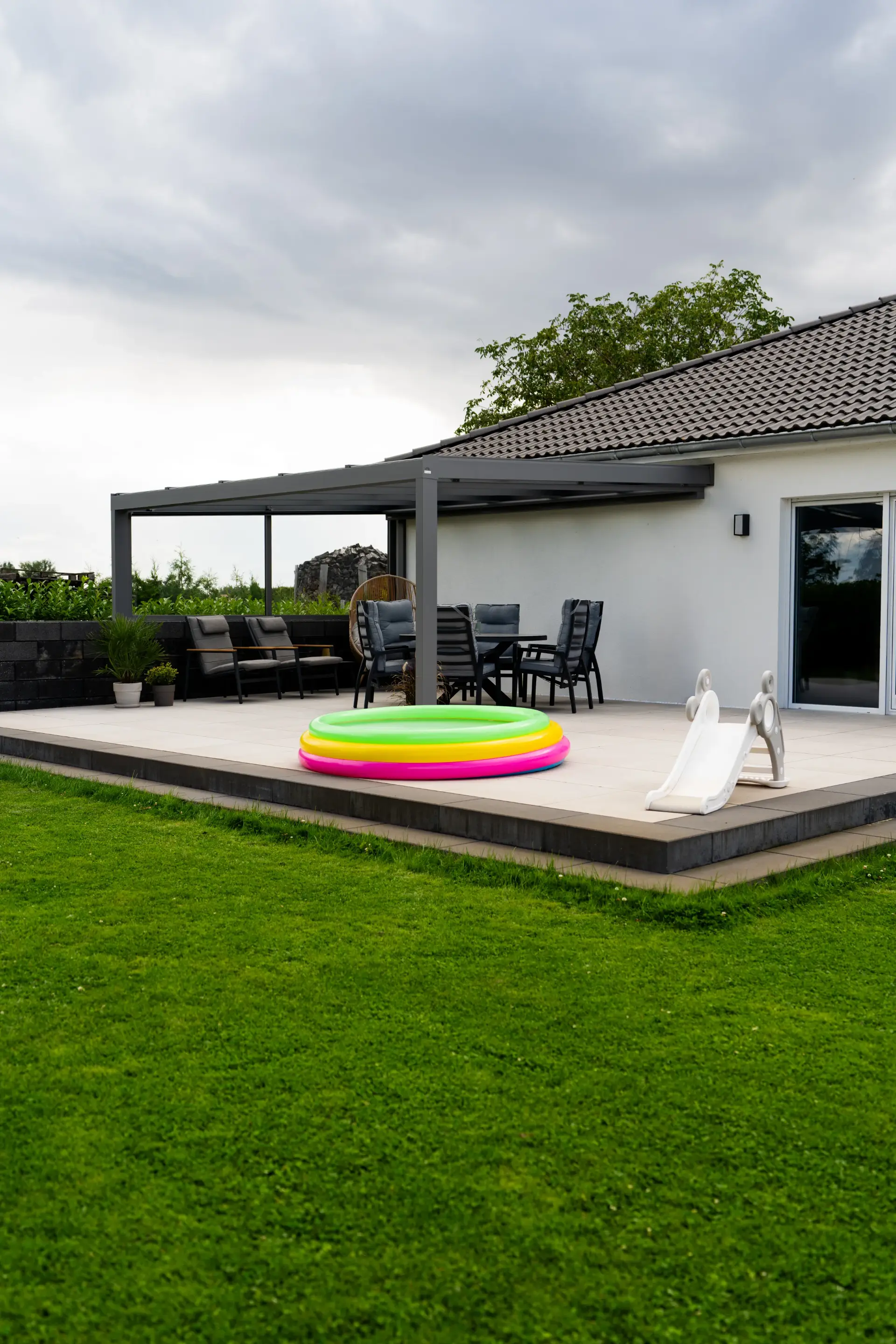 Terrassendach aus Aluminium in Anthrazit an einem Bungalow, darunter eine Sitzgruppe, davor ein Planschbecken auf der Terrasse