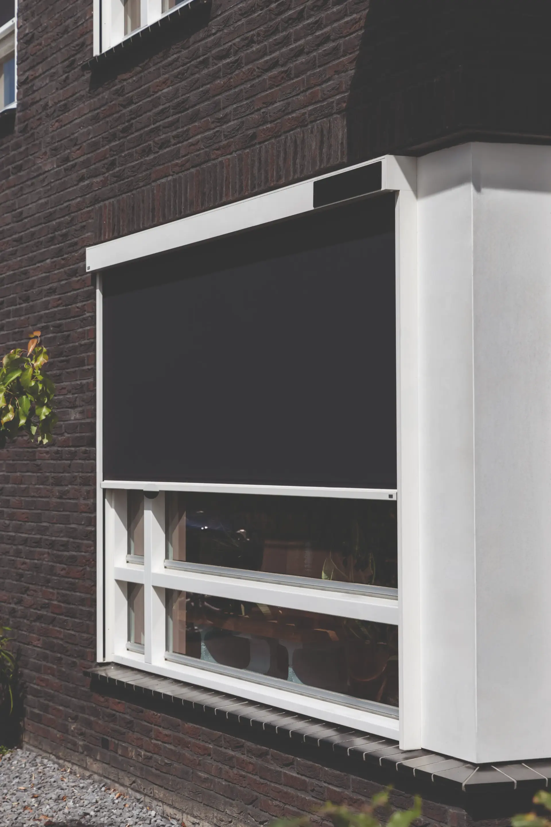 Weißer Vorbaukasten mit schwarzem Behang vor dem Fenster eines Klinkerhauses, der Sturz bleibt geschlossen