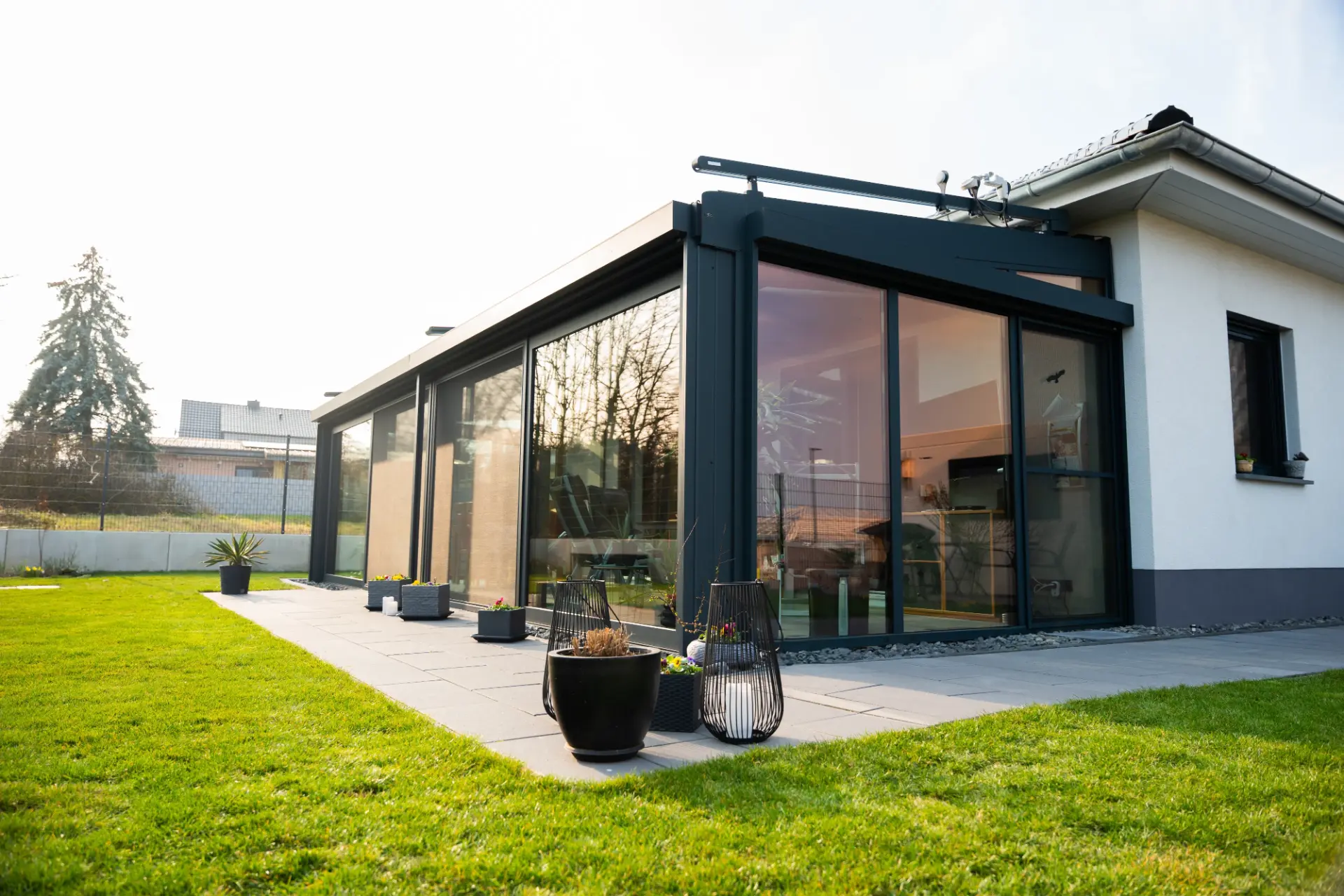 Wintergarten mit anthrazitfarbenen Aluminiumprofilen an einem Bungalow, davor Rasen und zwei Windlichter